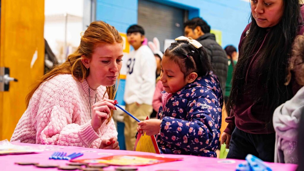 A woman is handing a young female student a pencil. The student is looking down at the pencil.